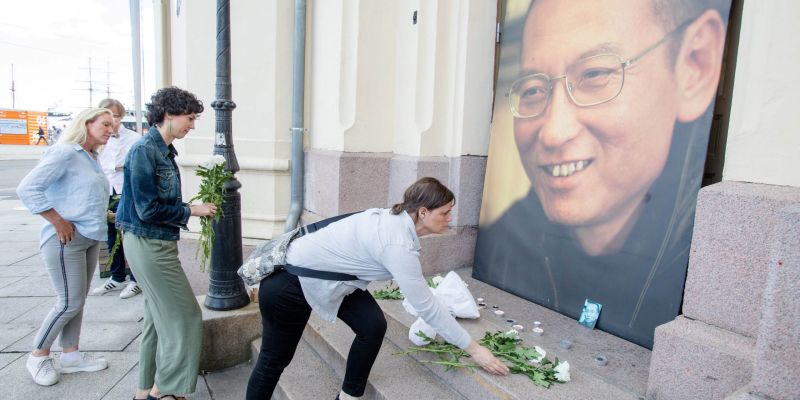 People place flowers and light candles in front a picture of late Nobel Peace Laureate Liu Xiaobo outside the Nobel Peace Center in Oslo