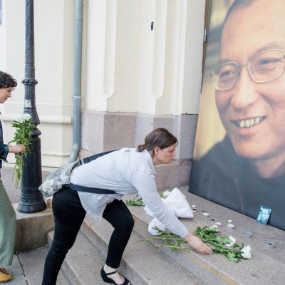 People place flowers and light candles in front a picture of late Nobel Peace Laureate Liu Xiaobo outside the Nobel Peace Center in Oslo
