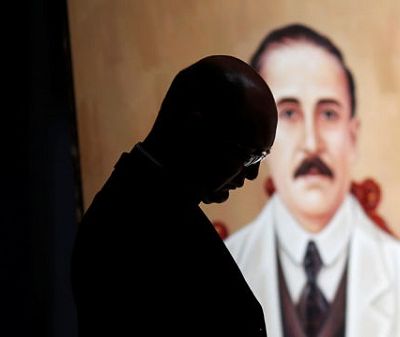 A priest stand in front of a painting depicting Jose Gregorio Hernandez during a mass in Caracas