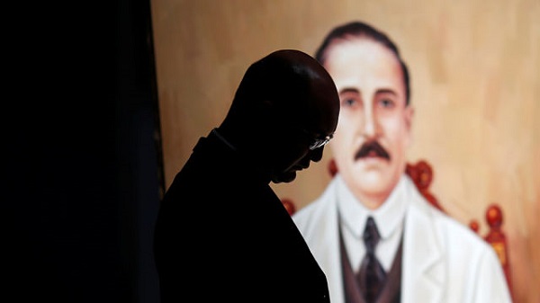 A priest stand in front of a painting depicting Jose Gregorio Hernandez during a mass in Caracas